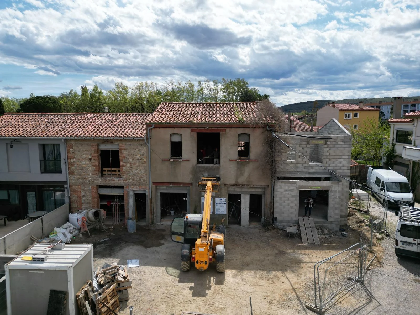 Bâtiment en cours de rénovation avec maçonneries apparentes, ouvertures sans menuiseries et engin de chantier