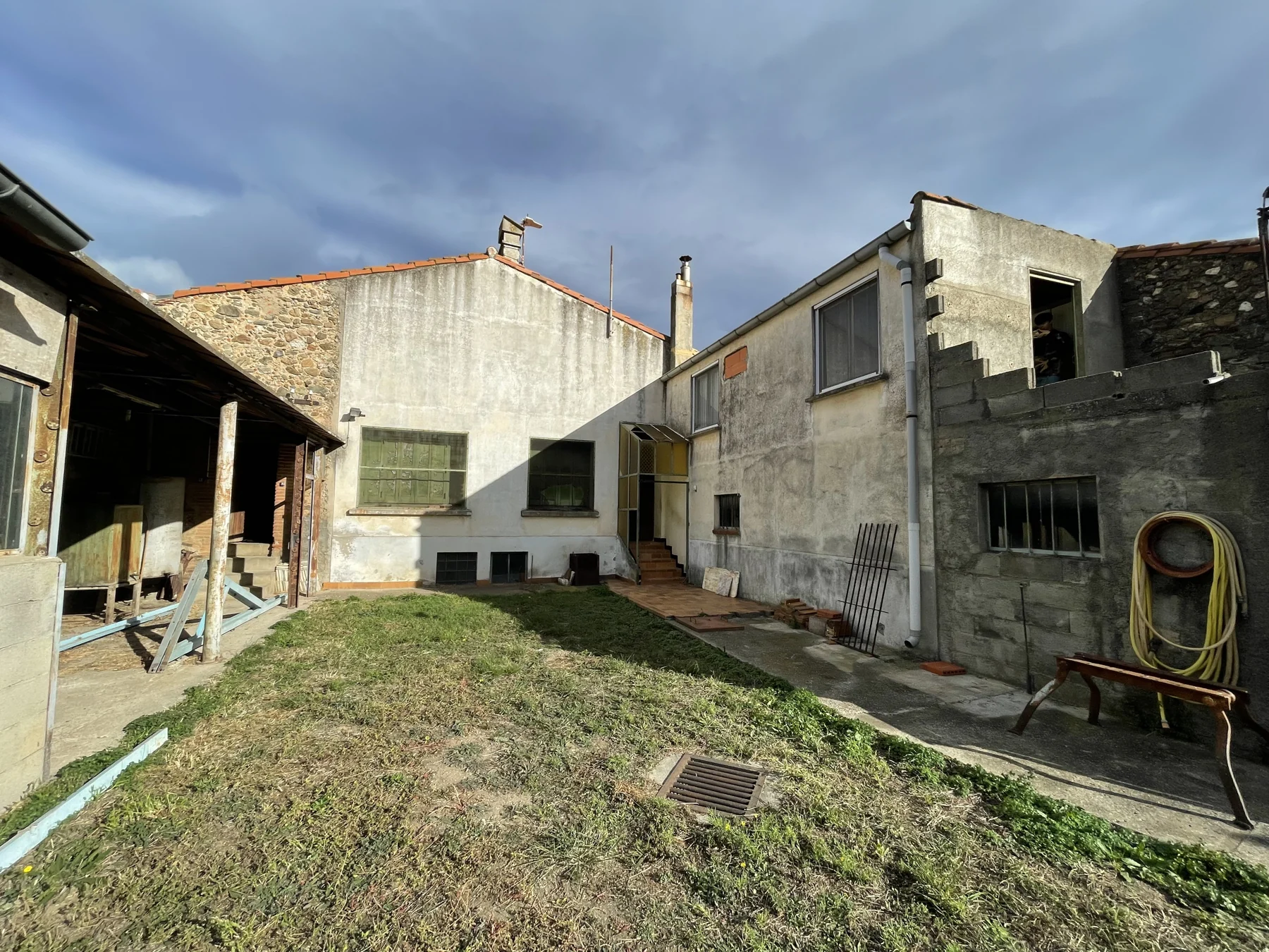 Cour avant rénovation, avec façades brutes, ancien appentis et terrain enherbé